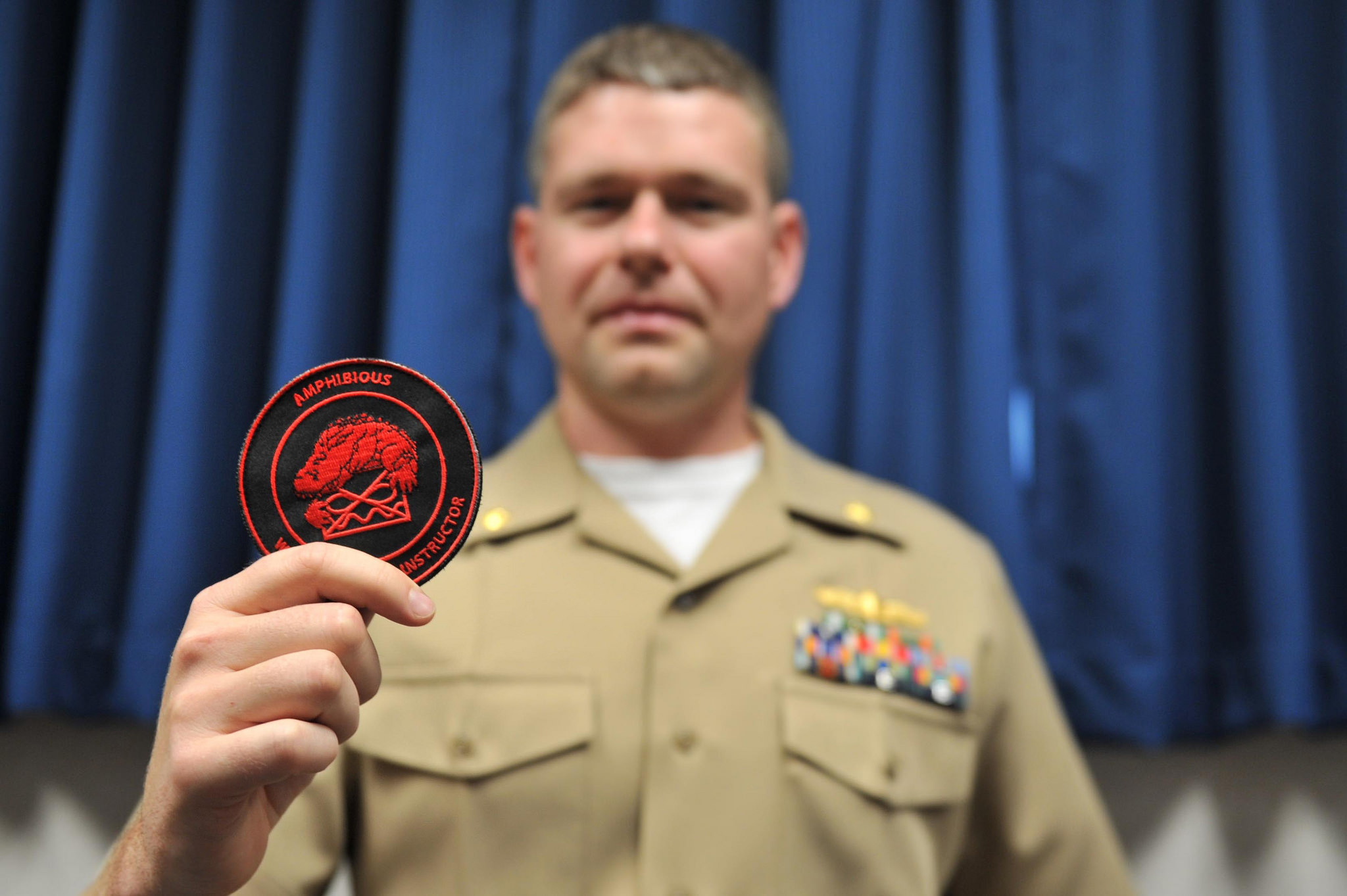 VIRGINIA BEACH, Va. (May 26, 2016) Lt. Cmdr. Dirk Sonnenberg, a graduate of Naval Surface and Mine Warfighting Development Center’s (SMWDC) Amphibious Warfare Tactics Instructor (WTI) course and winner of the course’s Iwo Jima Leadership Award, showcases the patch he and his classmates received upon graduating from the 14-week course. SMWDC is increasing the tactical proficiency of the surface warfare community by selecting elite surface warfare officers to become specialized warfighters called Warfare Tactics Instructors (WTI). (U.S. Navy photo by Mass Communication Specialist 2nd Class Jamie V. 